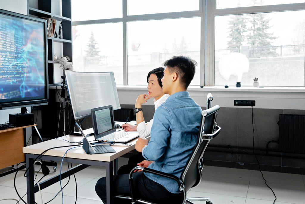 Engineers reviewing code and system architecture on a monitor in a modern collaborative workspace.