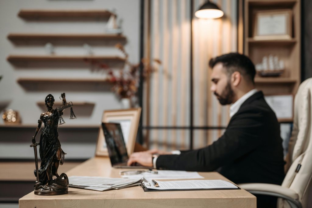 Attorney working at desk in modern law firm office reviewing documents on laptop